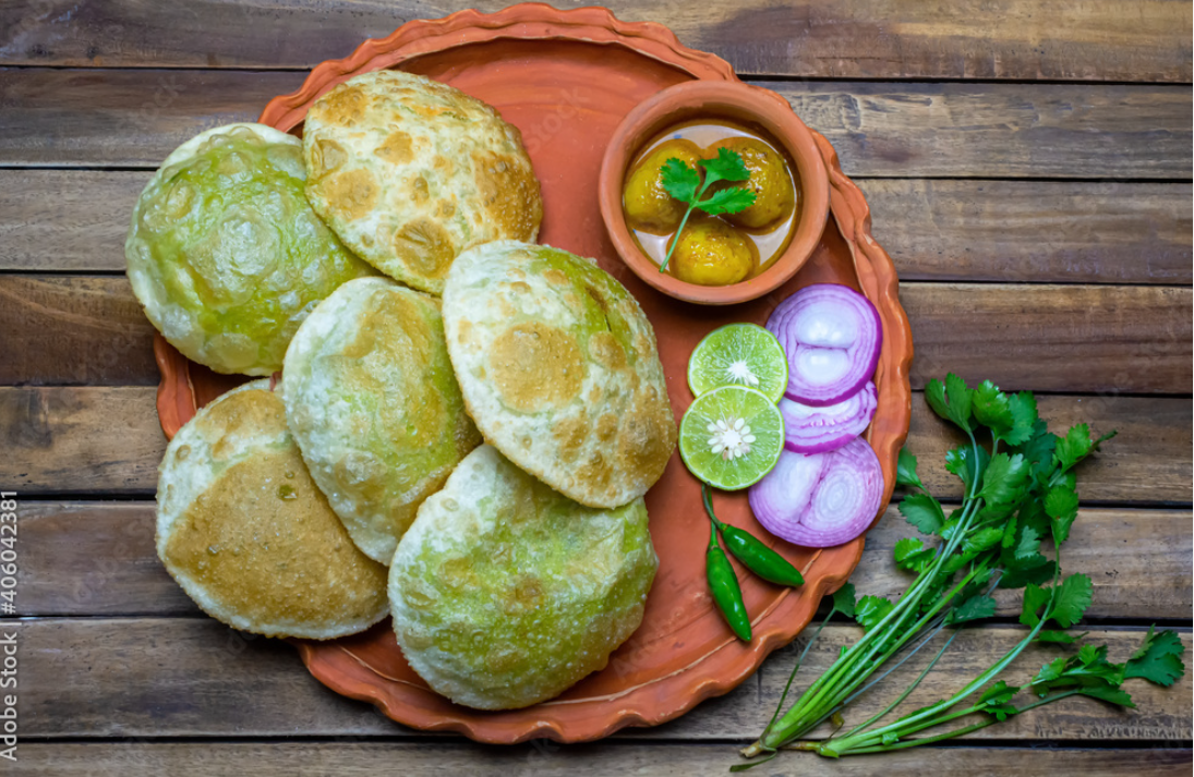 traditional bengali cuisine green peas kachori or koraishutir kochuri along with a bowl of spicy dum aloo curry onion lemon and green salad