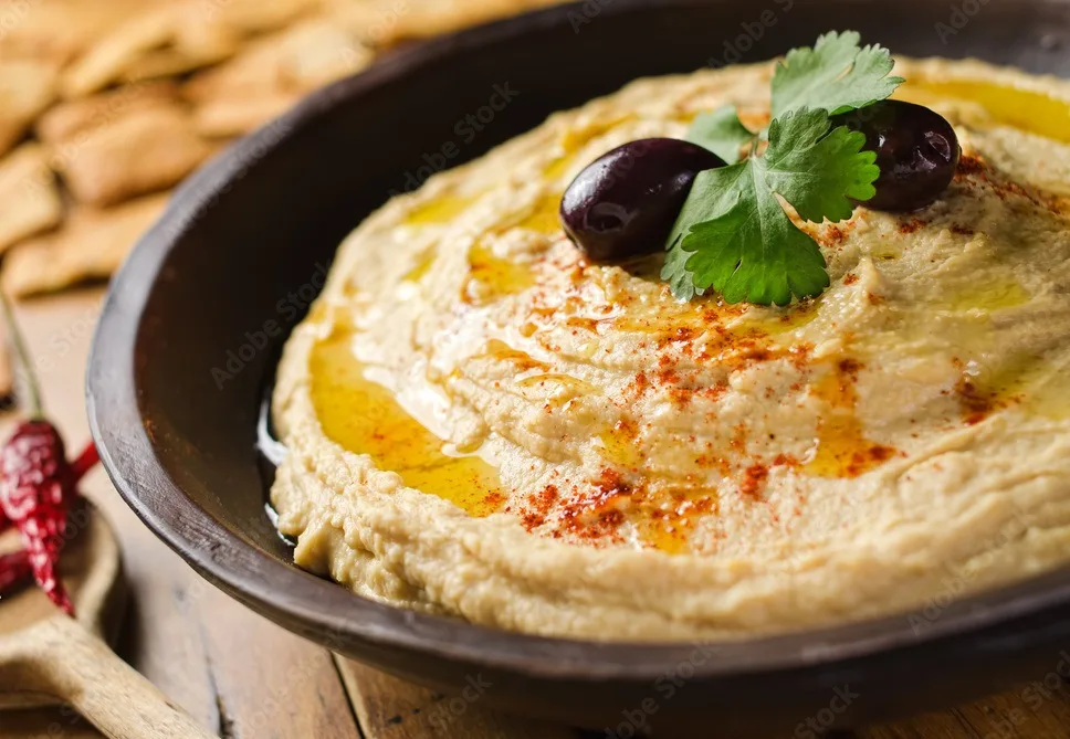 a bowl of creamy hummus with olive oil and pita chips.